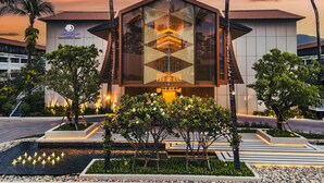 A modern hotel building with a glass facade, palm trees, and a landscaped garden.