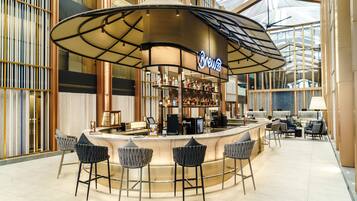 A bar area with a curved counter, bar stools, and a neon sign.
