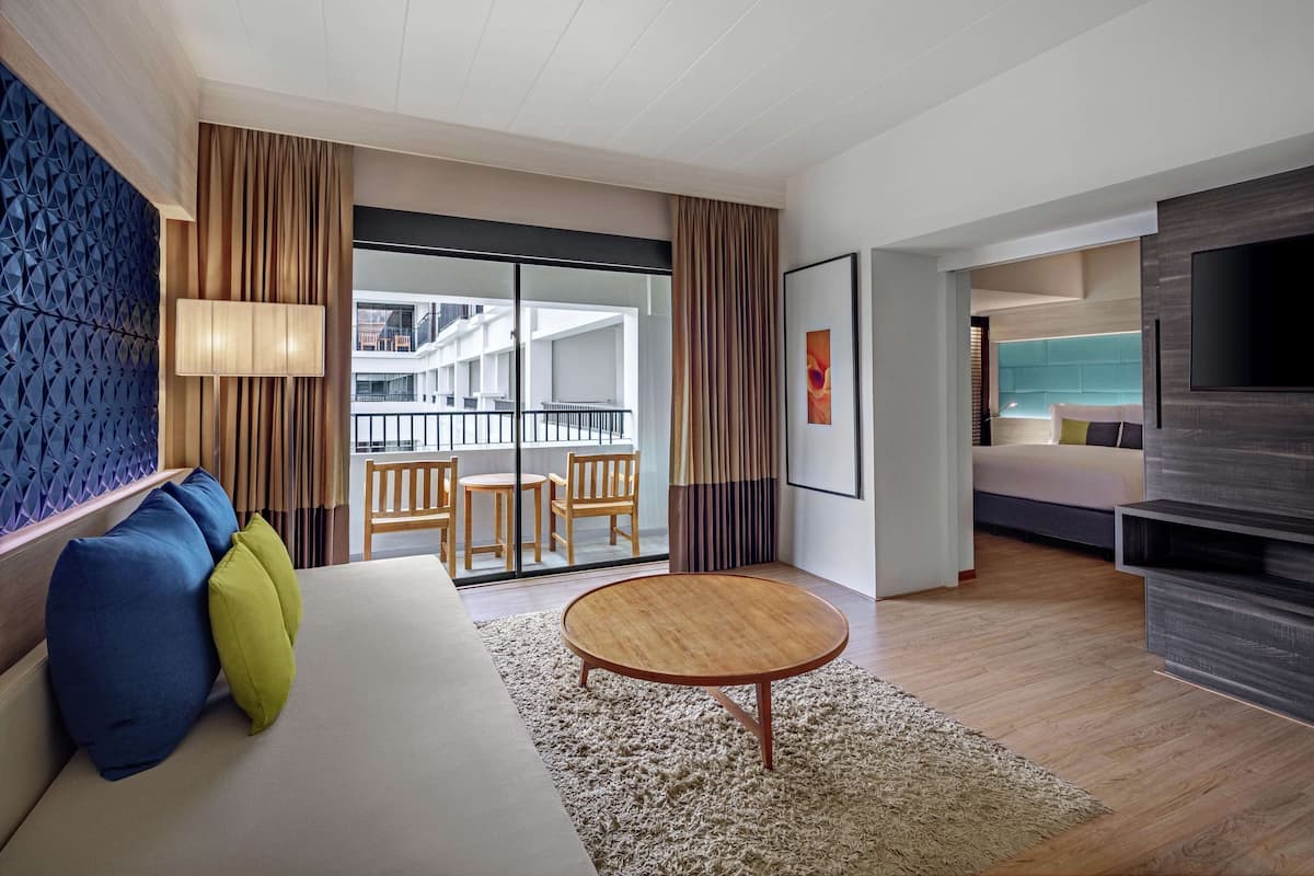Una habitación de hotel moderna con sofá, una mesita redonda y televisor. Tiene un balcón con vistas a la ciudad.