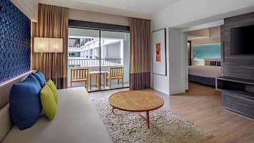 Une chambre d’hôtel moderne, dotée d’un canapé, d’une table basse ronde et d’un téléviseur. Elle dispose également d’un balcon avec vue sur la ville.