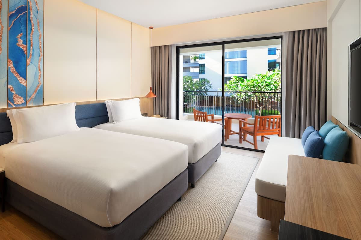 Habitación de hotel con dos camas, un sofá, una mesa de comedor y un balcón con vista a la ciudad.