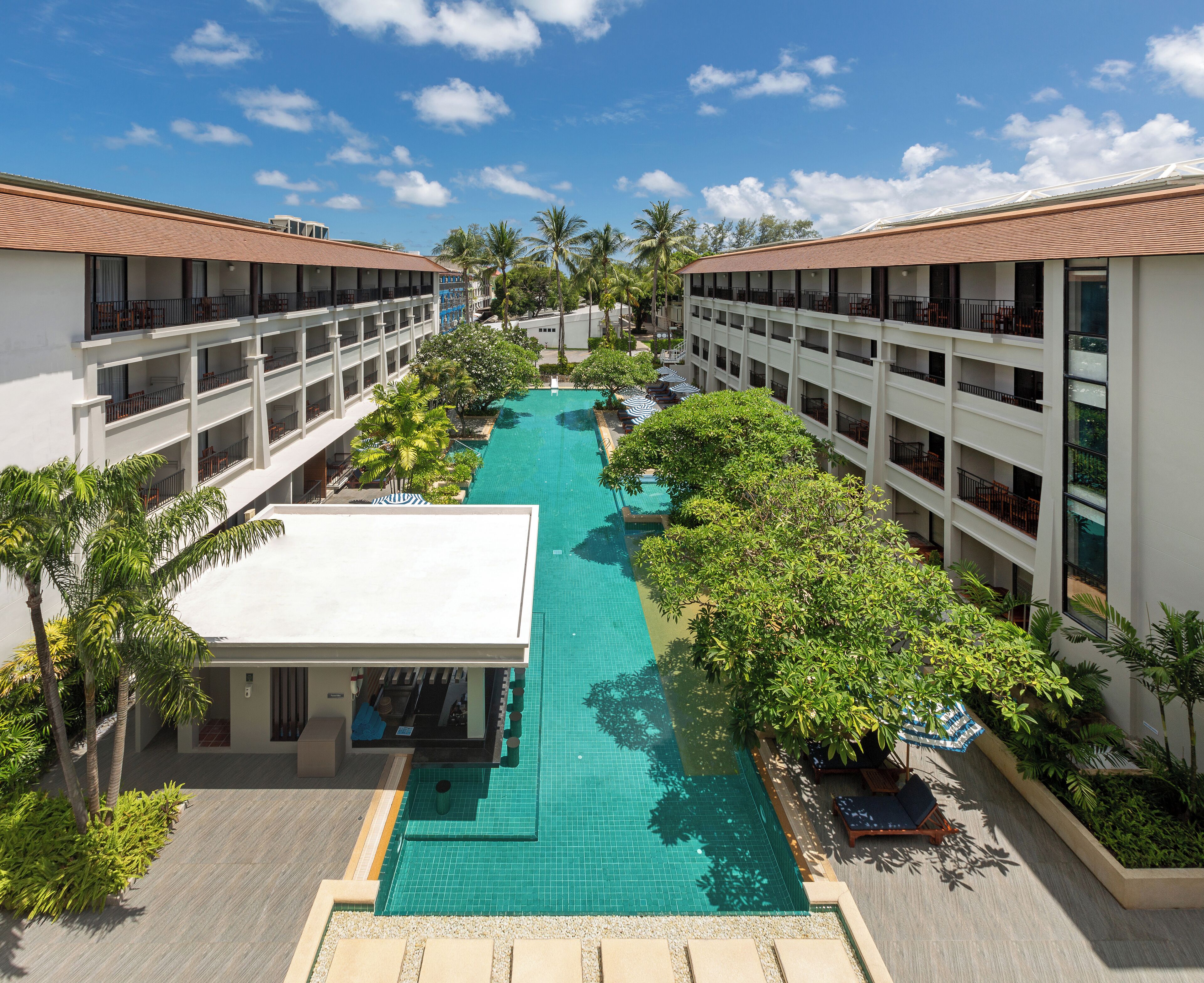 Ein Hotel mit einem zentralen Schwimmbad, mehreren Balkonen und üppiger Bepflanzung.