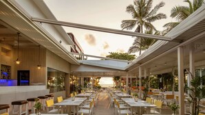 A spacious outdoor dining area with white tables and yellow chairs, overlooking a beach.