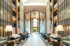 A spacious lobby with a high ceiling, a central seating area with sofas and chairs, and a large glass wall providing a view of the outdoors. - DoubleTree by Hilton Phuket Banthai Resort (Patong)