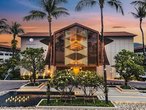 A modern hotel building with a distinctive geometric glass facade, surrounded by palm trees and a landscaped garden. - DoubleTree by Hilton Phuket Banthai Resort (Patong)