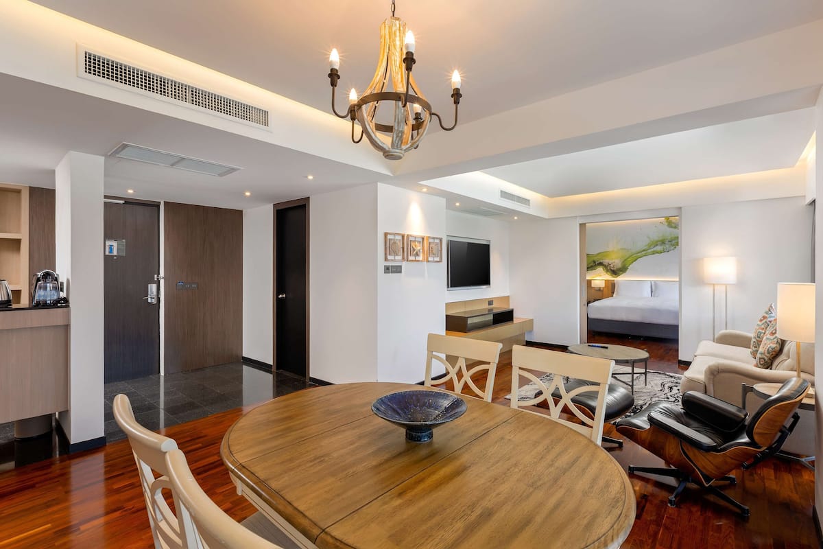 Una habitación de hotel moderna con comedor, sala de estar con sofá y televisor, y entrada independiente.