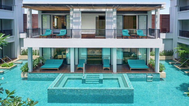 A two-story hotel with a rooftop pool, outdoor seating, and a glass-enclosed lounge area.