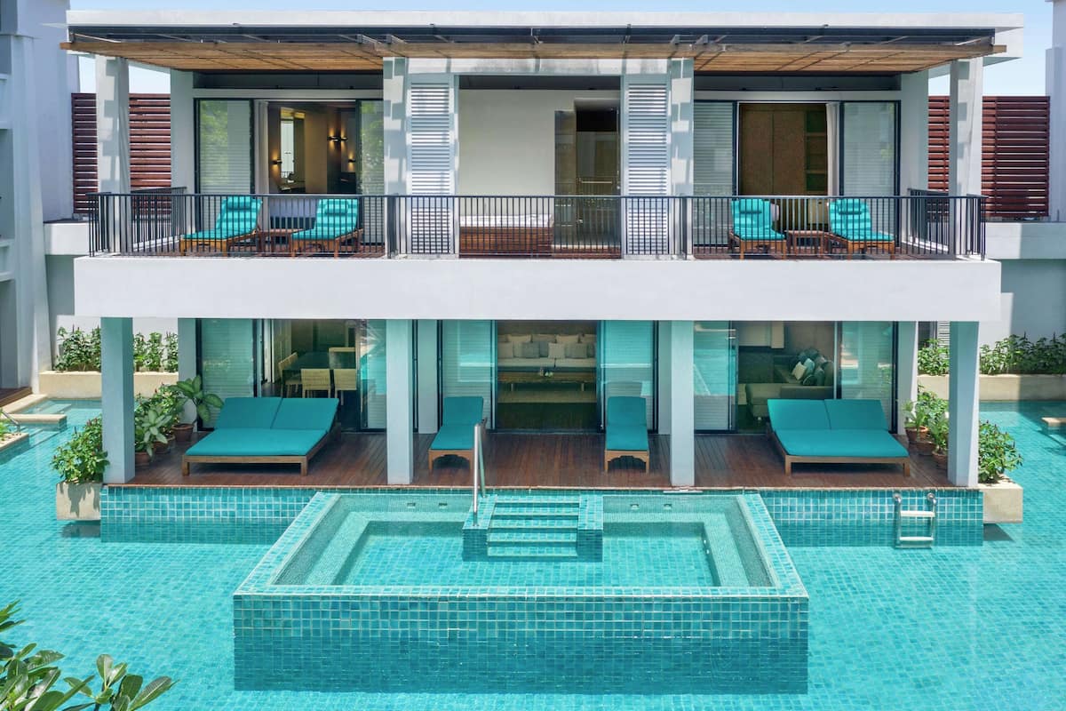 Un hotel de dos pisos con piscina en la azotea, asientos exteriores y un área de lounge con paredes de vidrio.
