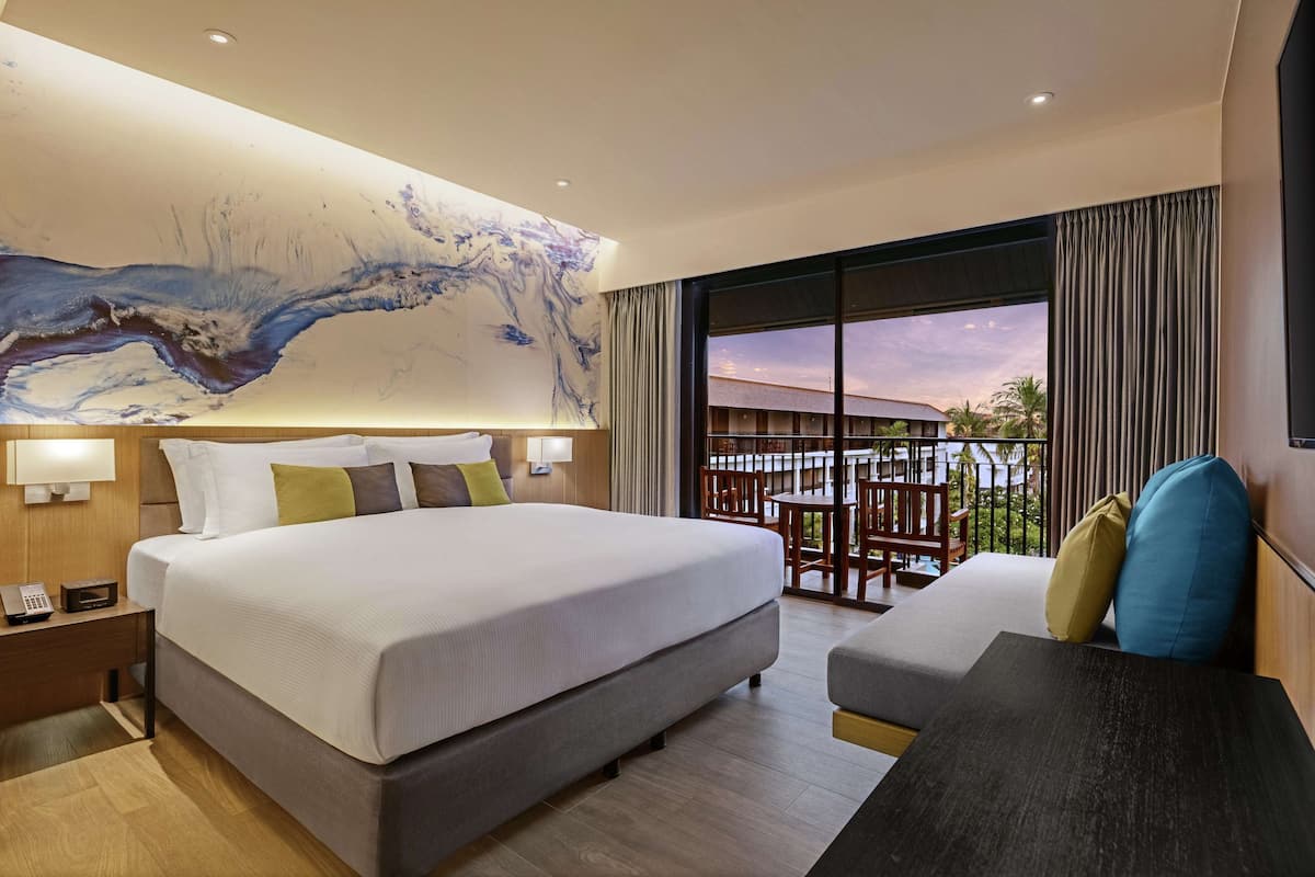 Una habitación de hotel moderna con una cama grande, un escritorio y un balcón con vistas al atardecer.