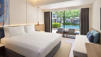 Habitación de hotel con una cama grande, un sofá, un escritorio y vistas a una piscina y zona de estar al aire libre.