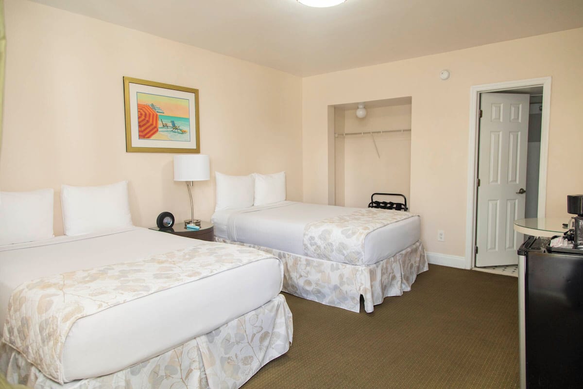 A hotel room with two beds, a nightstand, a lamp, a door, and a painting on the wall.
