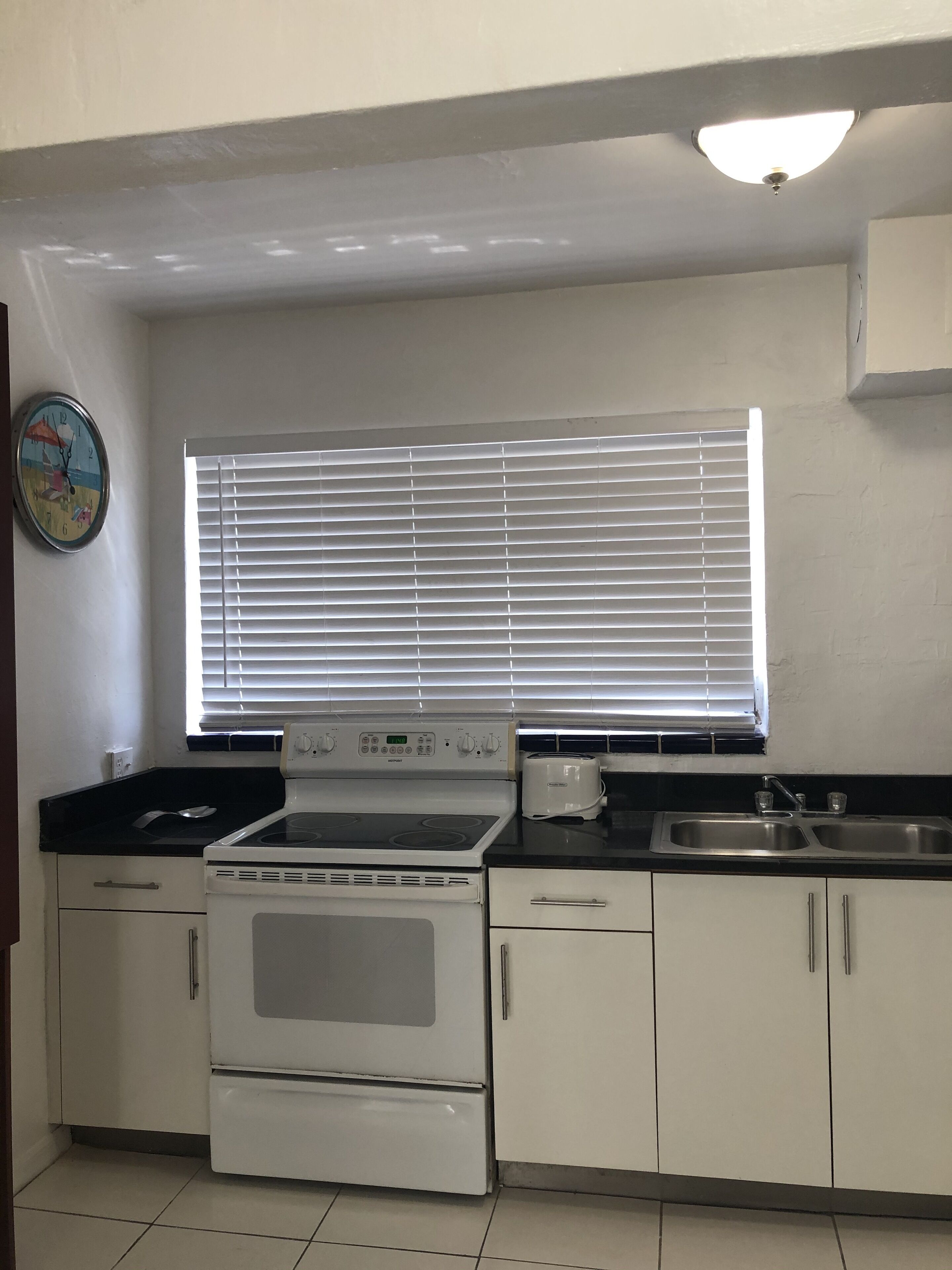 A kitchen with a stove, oven, sink, and window blinds.