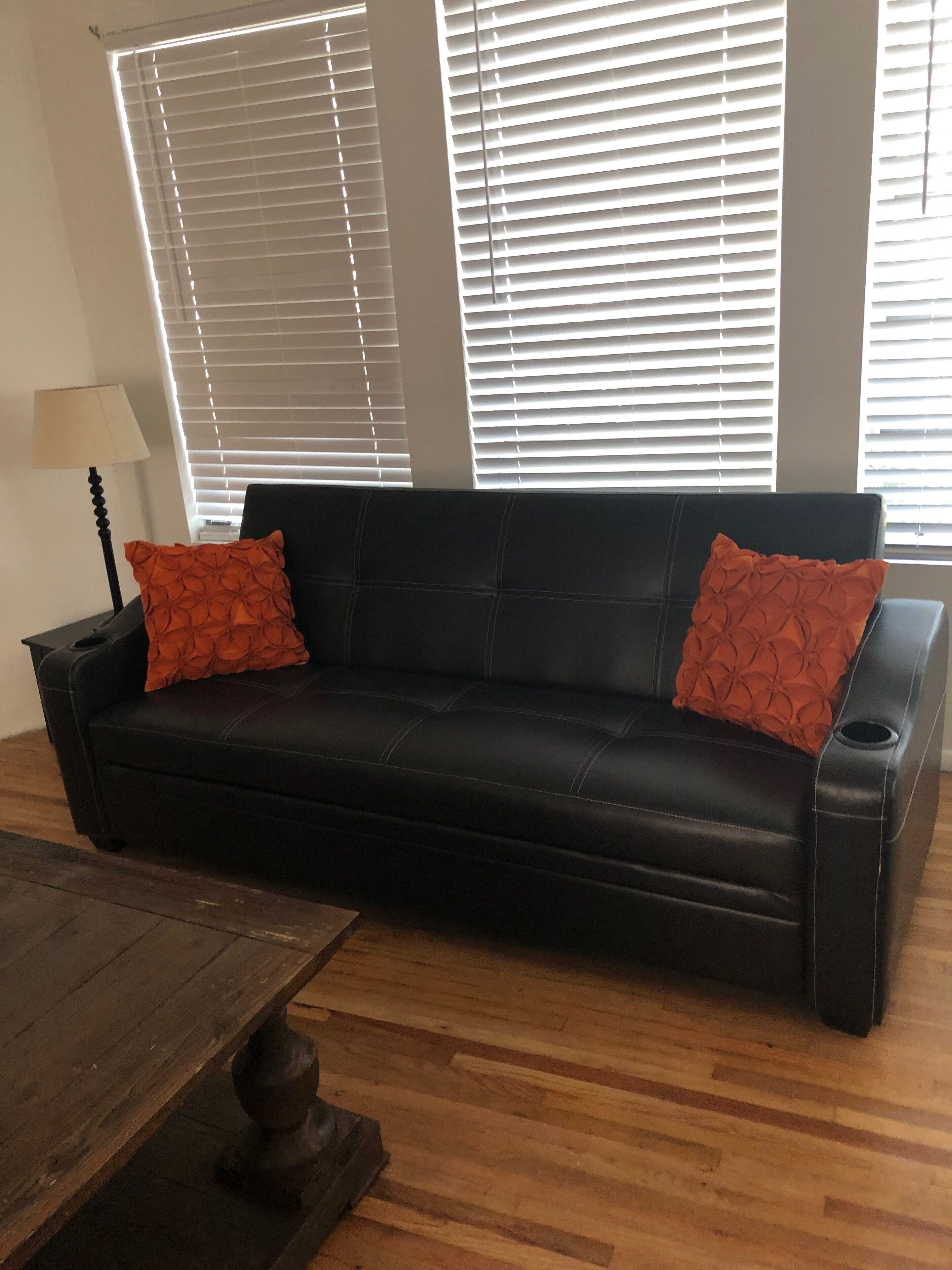 A black leather sofa with orange cushions, a wooden coffee table, and a lamp.