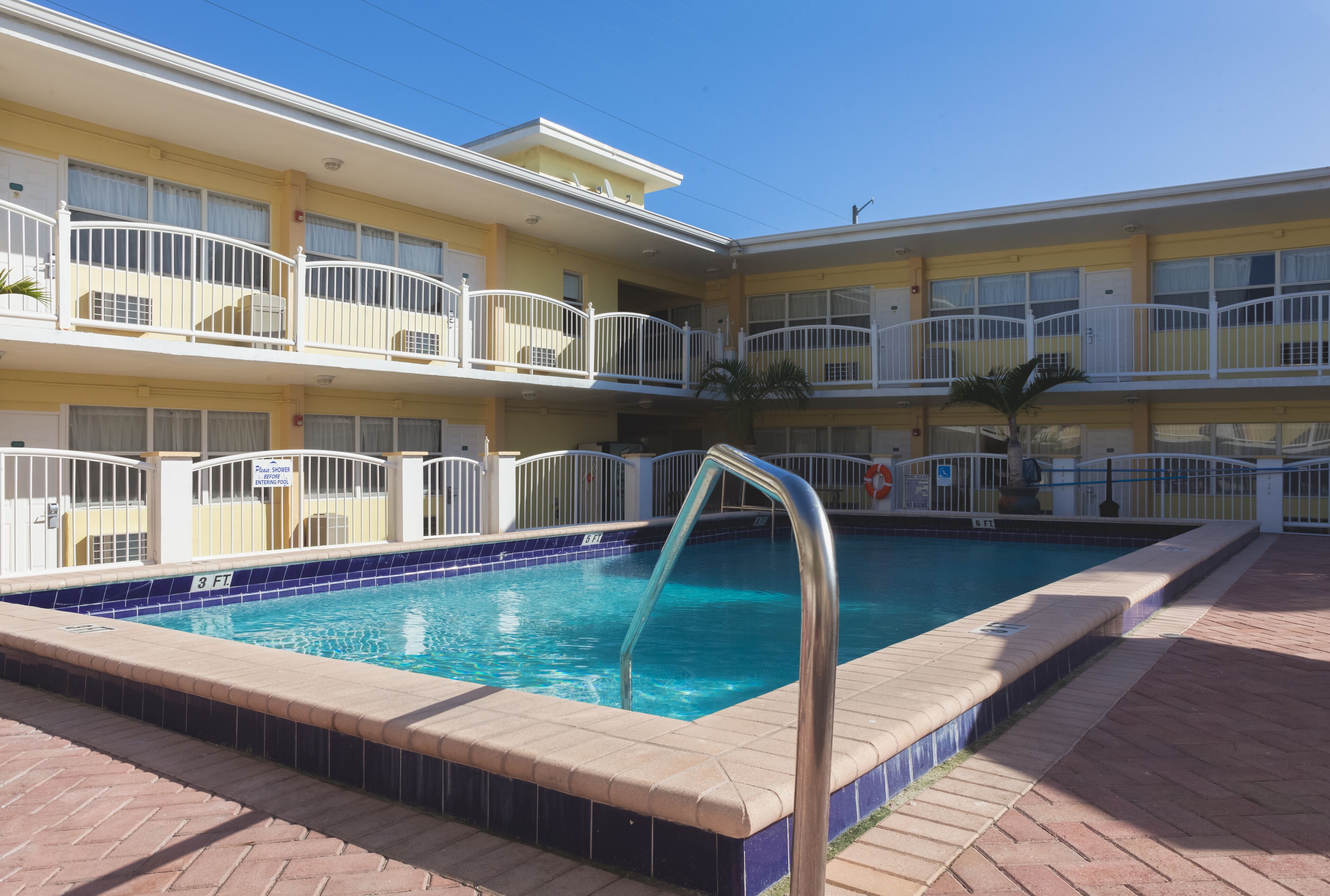 A hotel with a pool area, including a pool with a metal ladder, a brick walkway, and a two-story building with balconies.