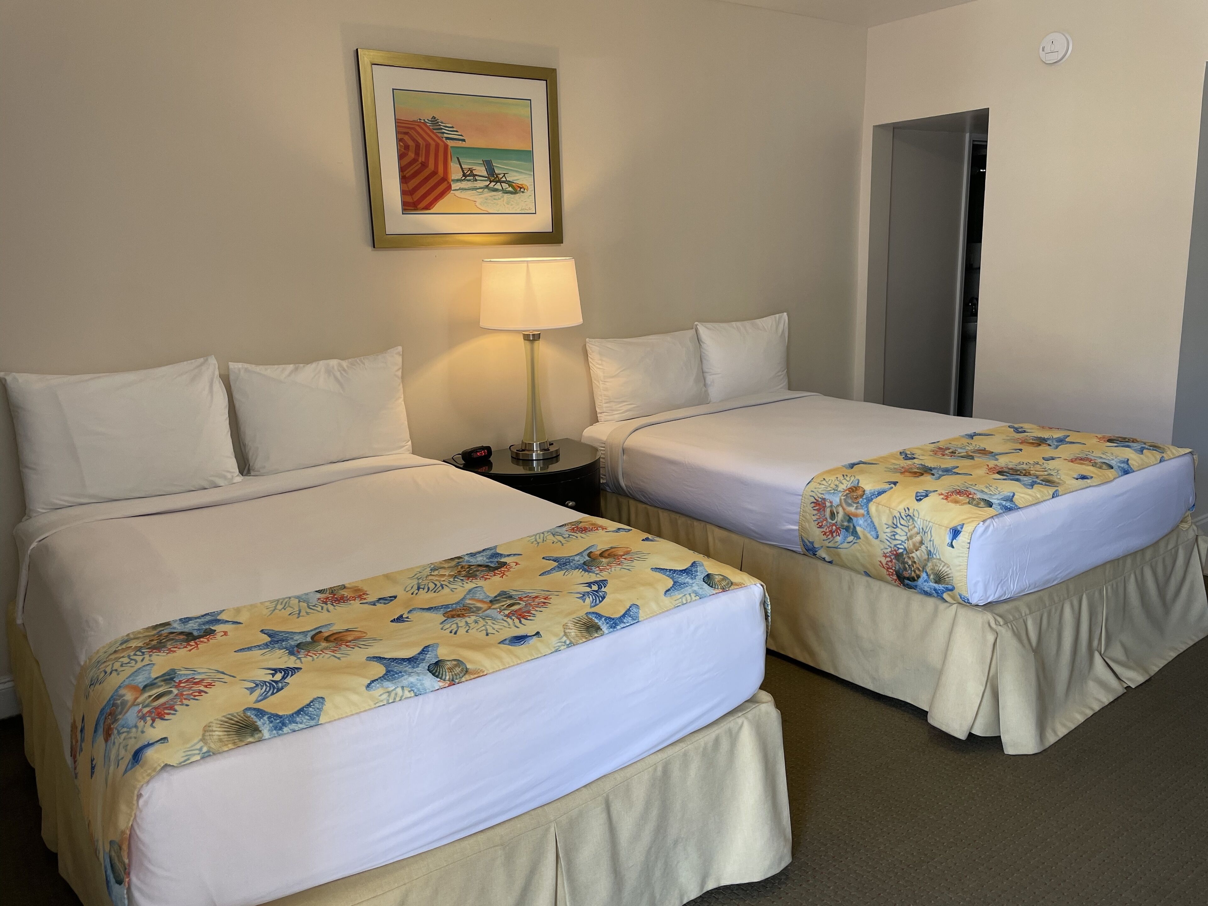 Une chambre d’hôtel avec deux lits, chacun recouvert d’une couvre-lit à motifs floraux, une lampe de chevet et un tableau encadré au mur.