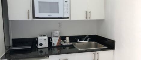 A compact kitchen with white cabinets, a microwave, a toaster, a coffee maker, and a sink.
