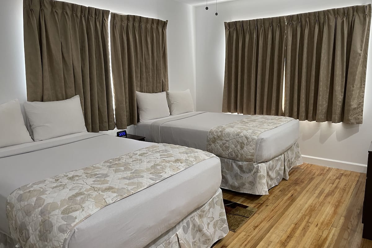 A hotel room with two beds, a wooden floor, and brown curtains.
