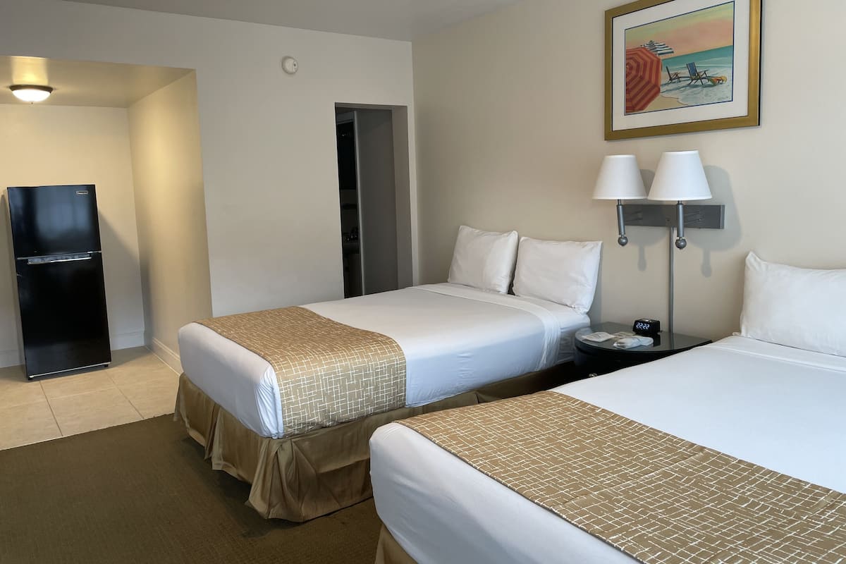A hotel room with two beds, a refrigerator, a nightstand with a lamp, and a painting on the wall.