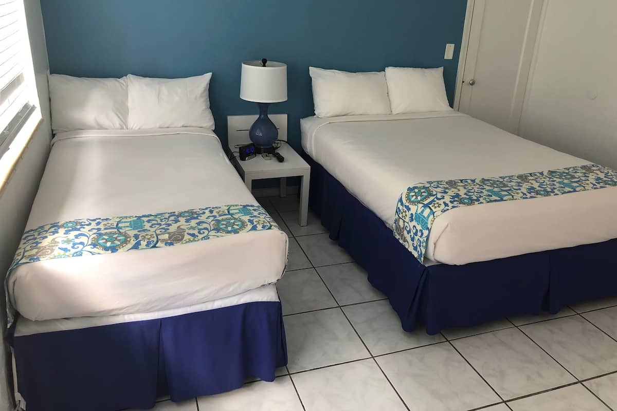 A hotel room with two beds, a nightstand with a lamp, and a door.