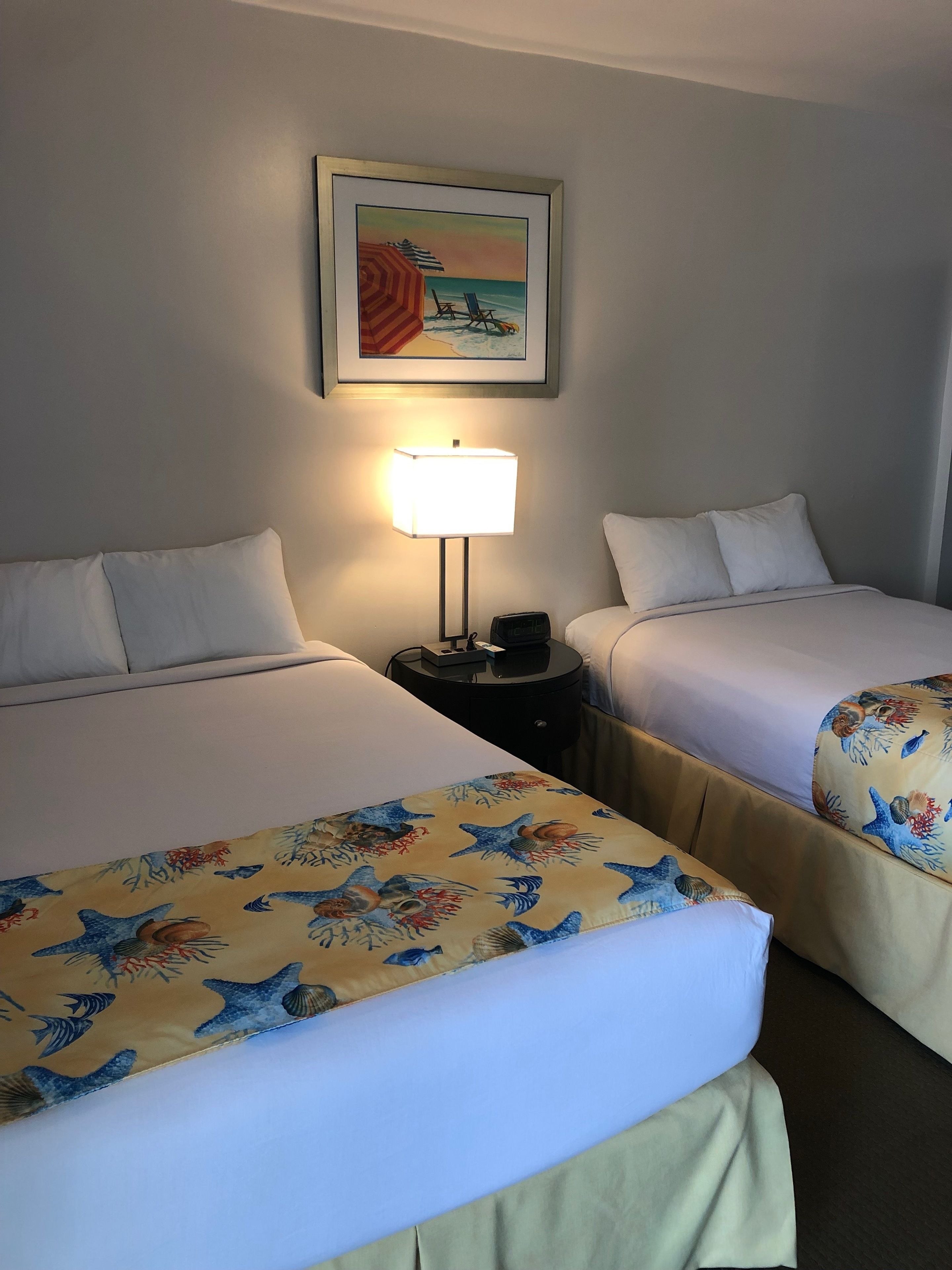 Ein Hotelzimmer mit zwei Betten, einem Nachttisch mit Lampe und einem gerahmten Bild an der Wand.
