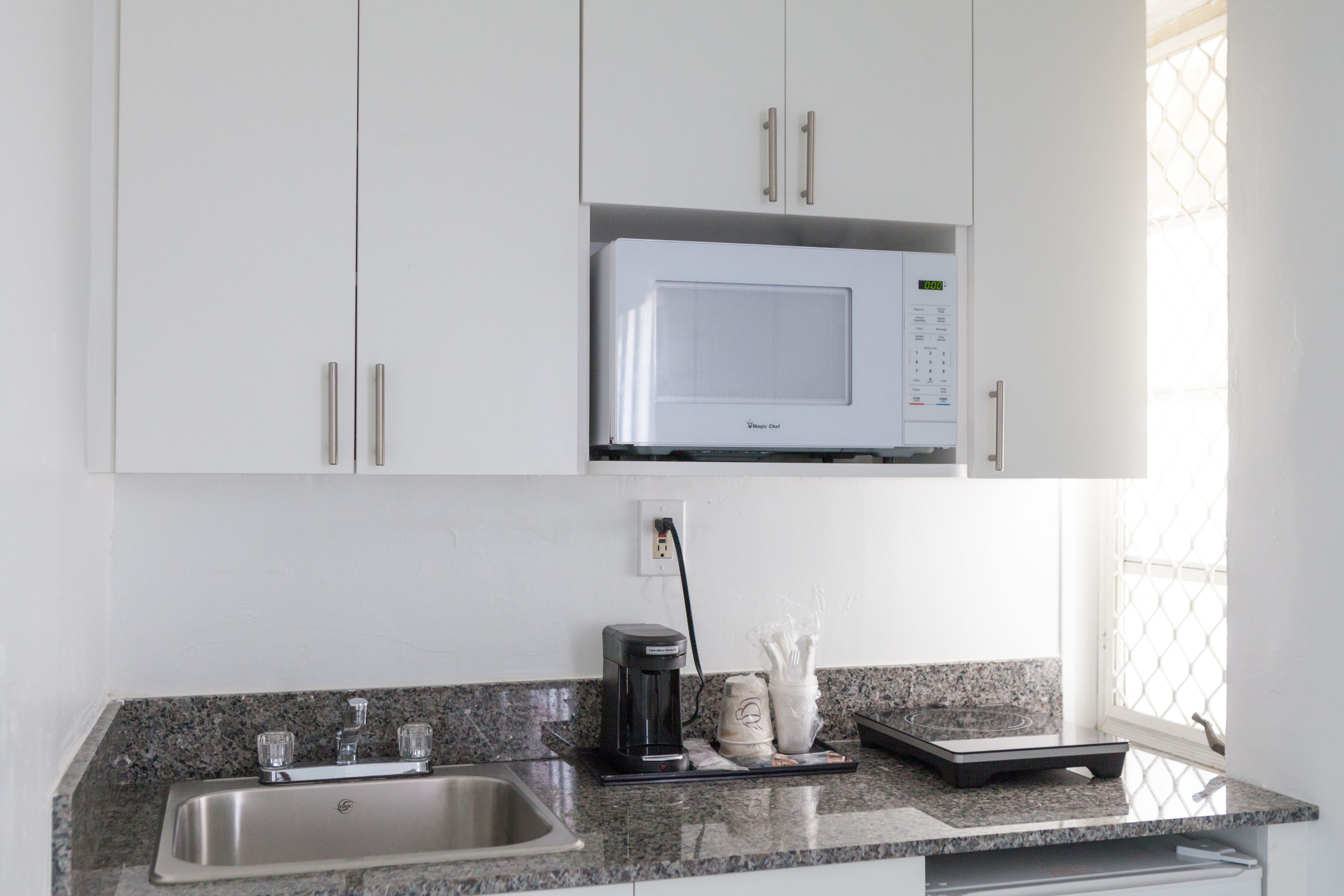 A kitchen with white cabinets, a stainless steel sink, a microwave, and a coffee maker.