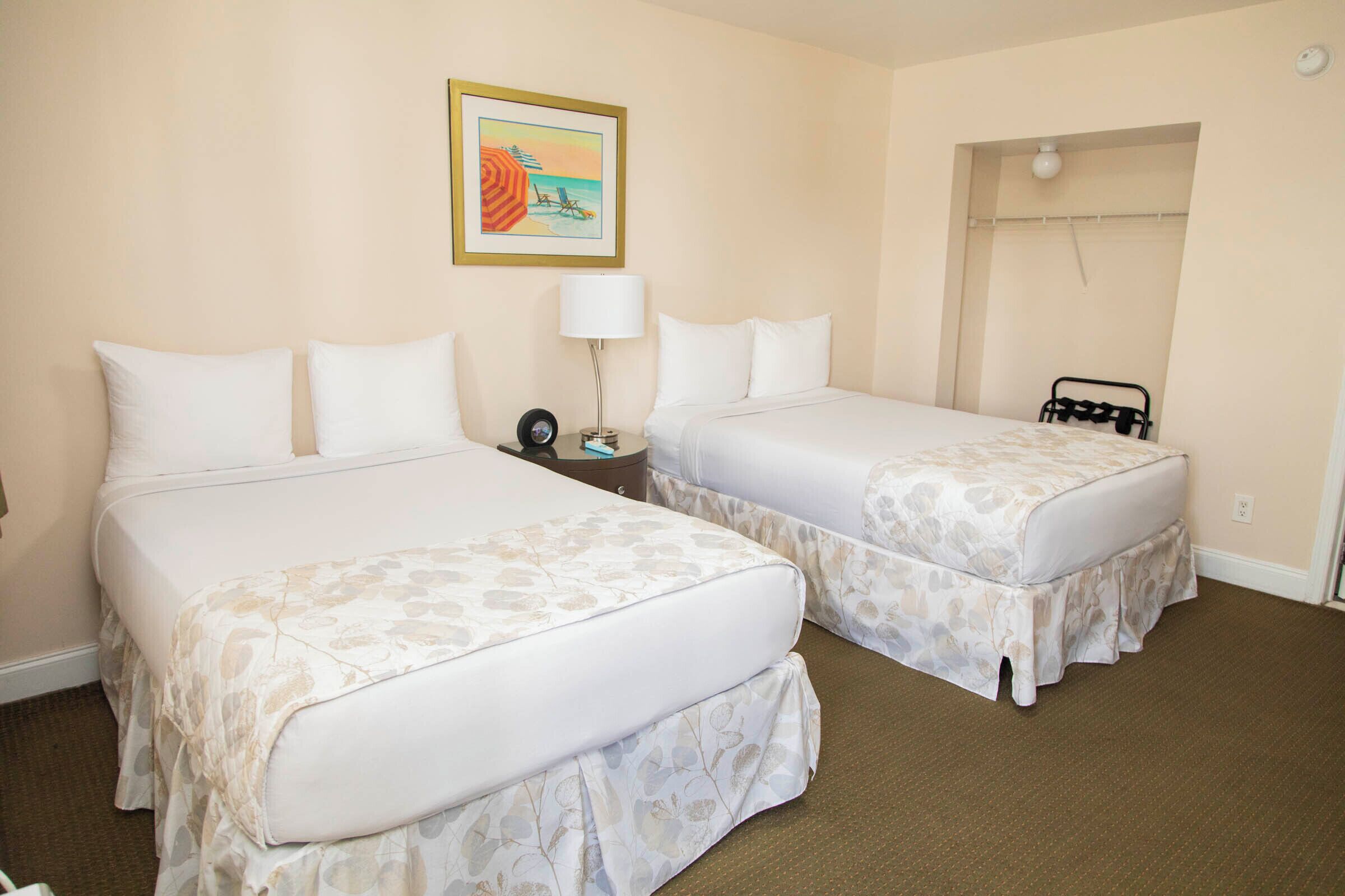 A hotel room with two beds, a nightstand, a lamp, a painting, and a closet with a mirror.