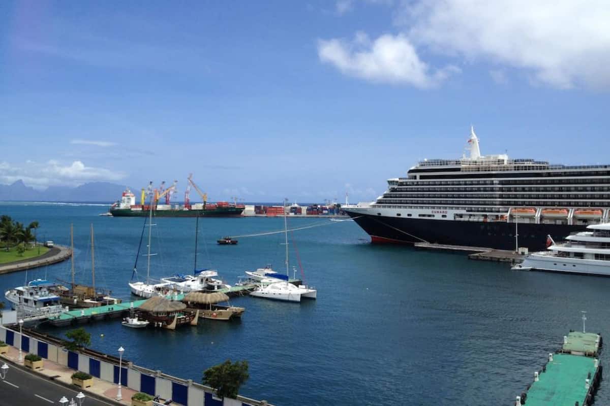 A cruise ship docked at a port with smaller boats and a clear view of the coastline.