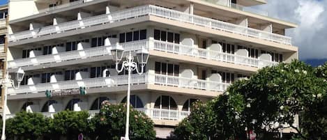Un hotel de varios pisos con balcones, vista a la calle y coches aparcados.