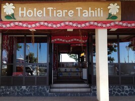 The exterior of Hotel Tiare Tahiti with a wooden signboard, large windows, and a red floral border.
