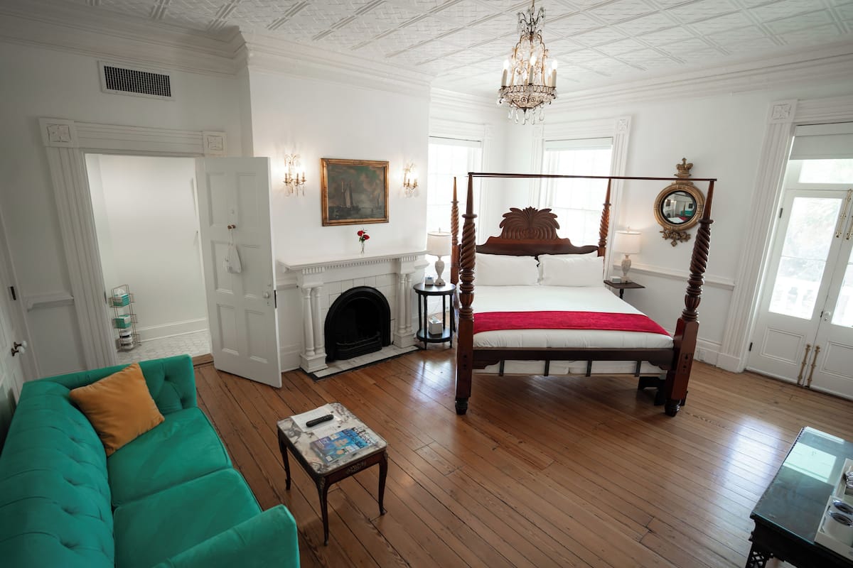 A spacious room with a four-poster bed, a fireplace, a teal sofa, and a wooden floor.