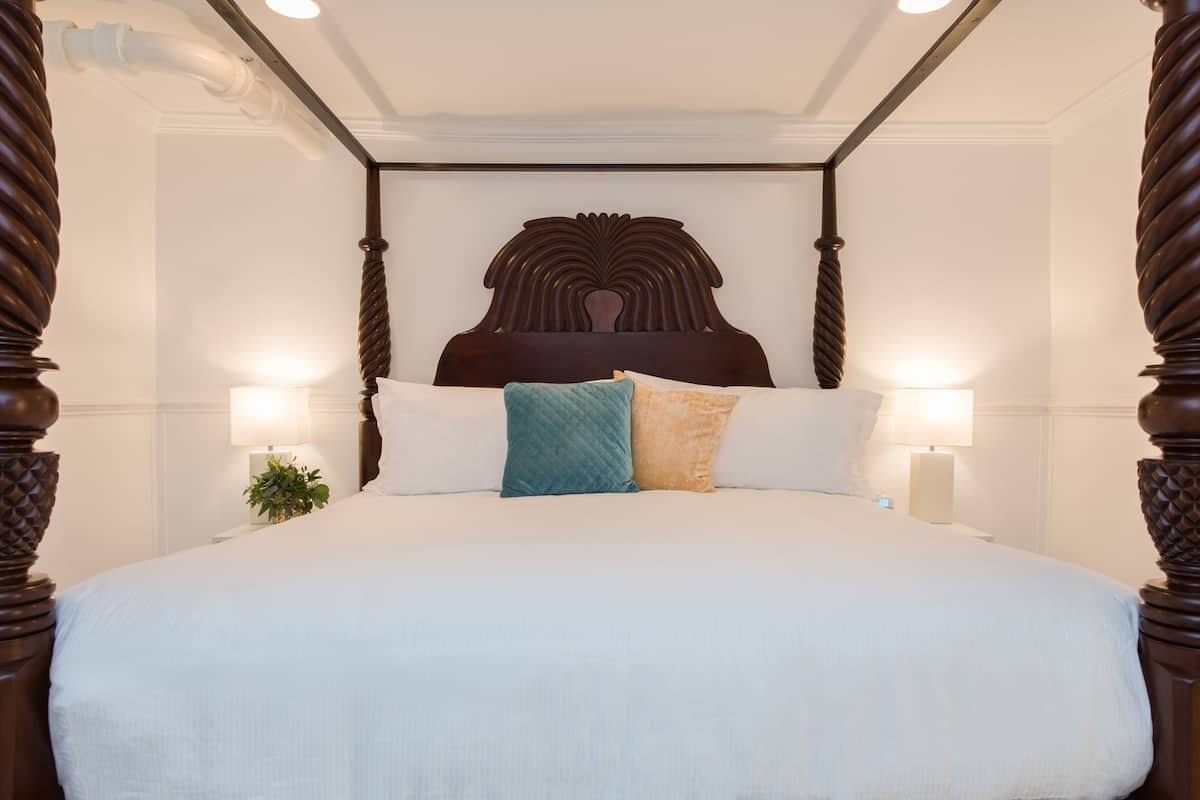 A four-poster bed with a dark wooden headboard, white linens, and two bedside lamps.