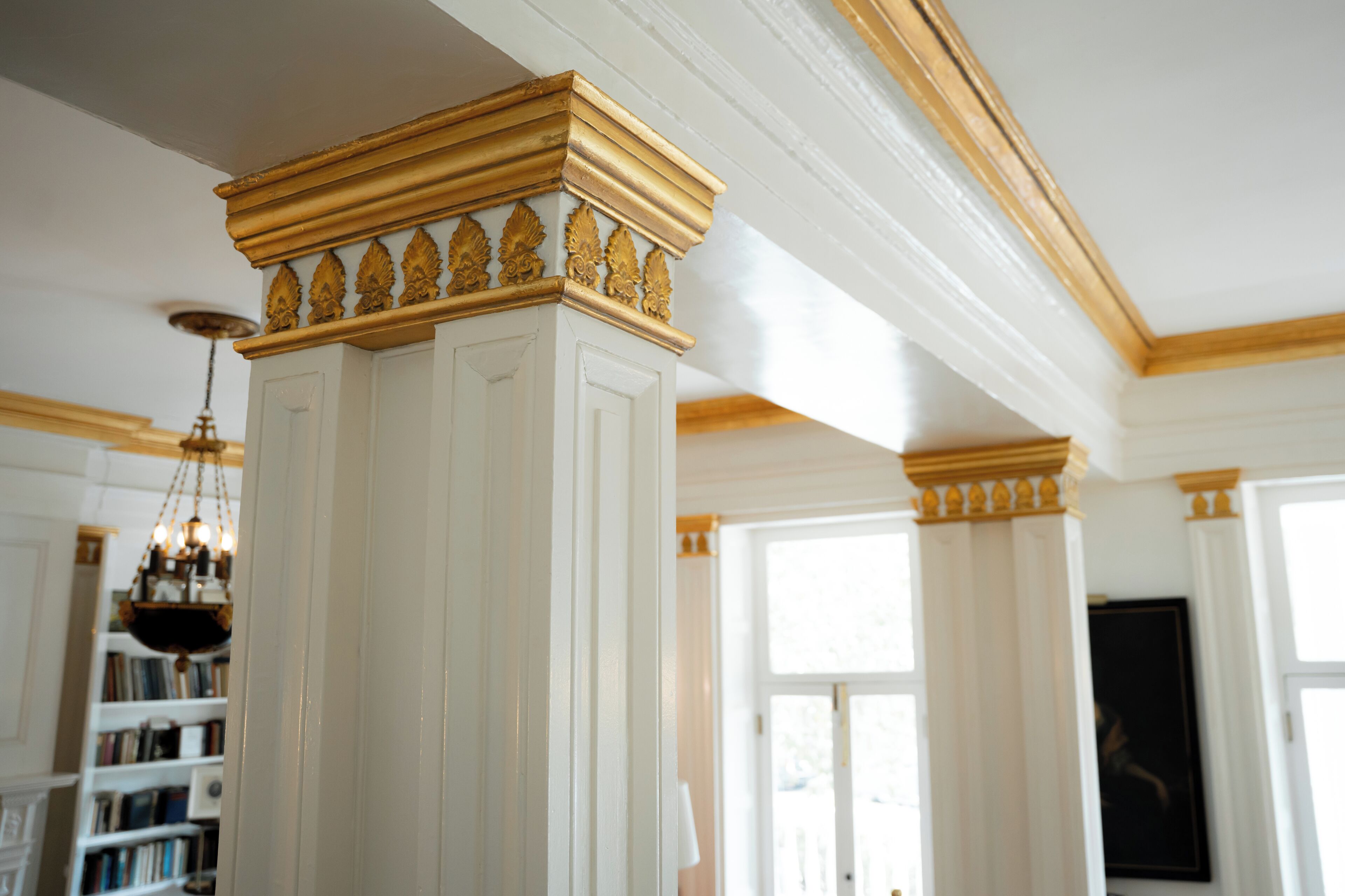 Et værelse med en hvid søjle med guld detaljer, en lysekrone og en reol i baggrunden.
