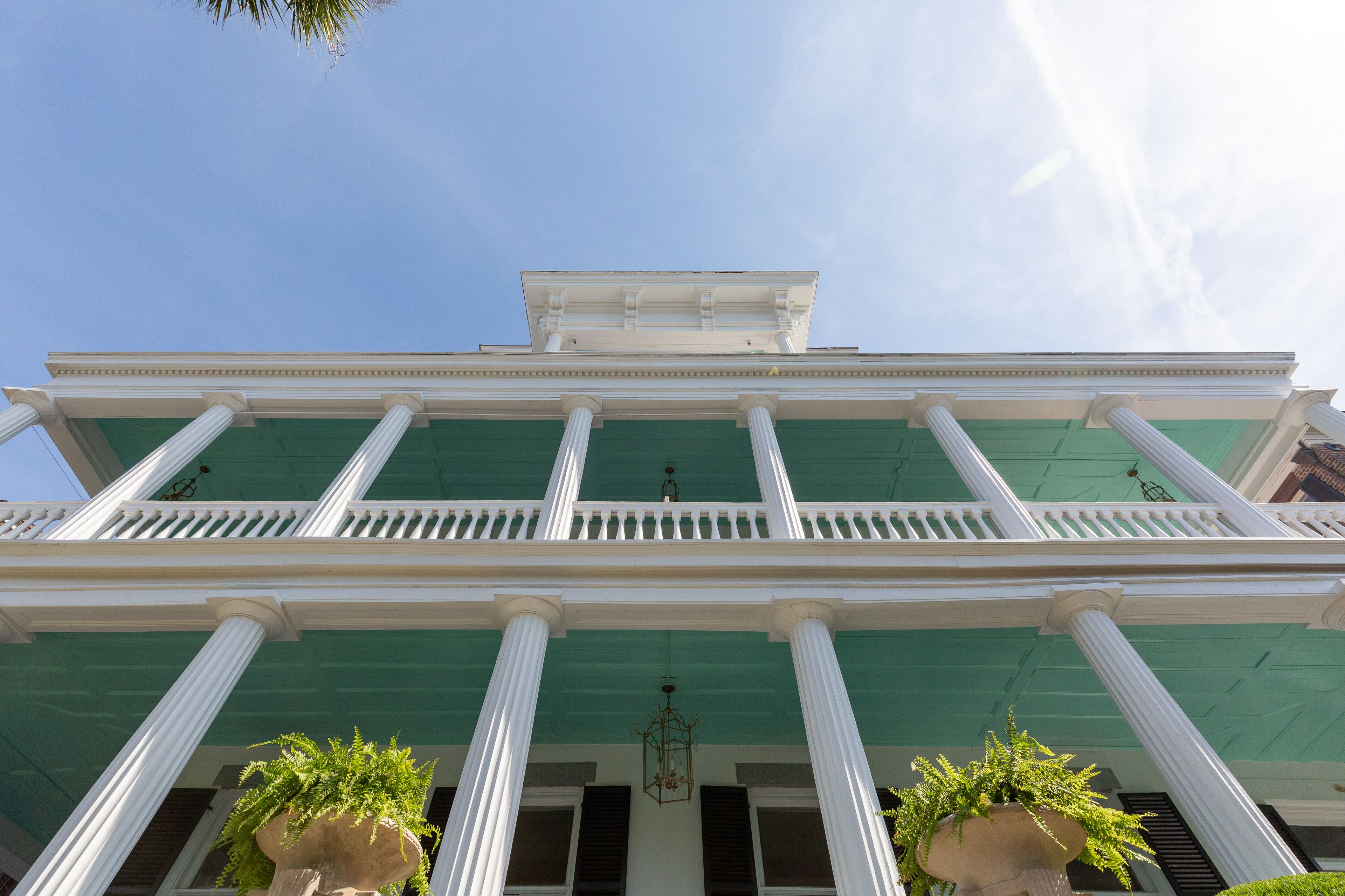 Un edificio con tetto verde, colonne bianche e un balcone con ringhiere bianche.