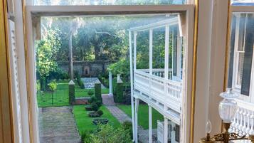 Una habitación con vistas a un jardín a través de una ventana, una barandilla blanca y una mesa con una lámpara.