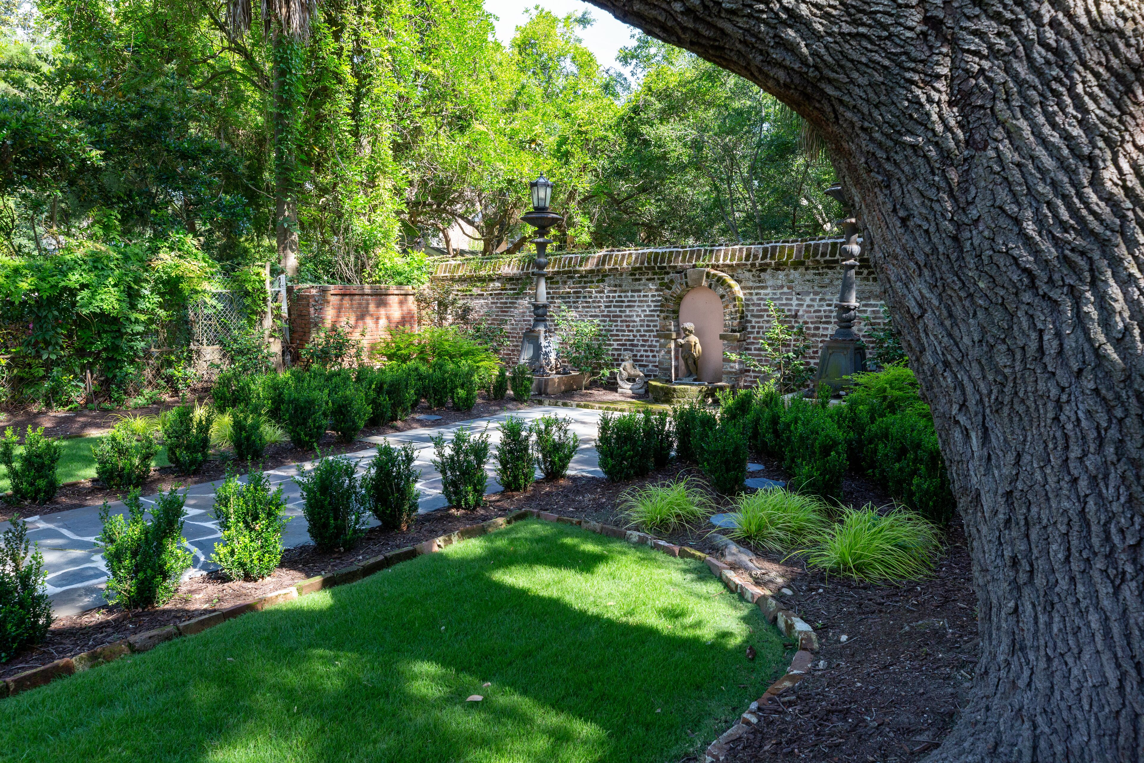 Un jardín ajardinado con un sendero pavimentado, setos bien recortados y un muro de piedra.
