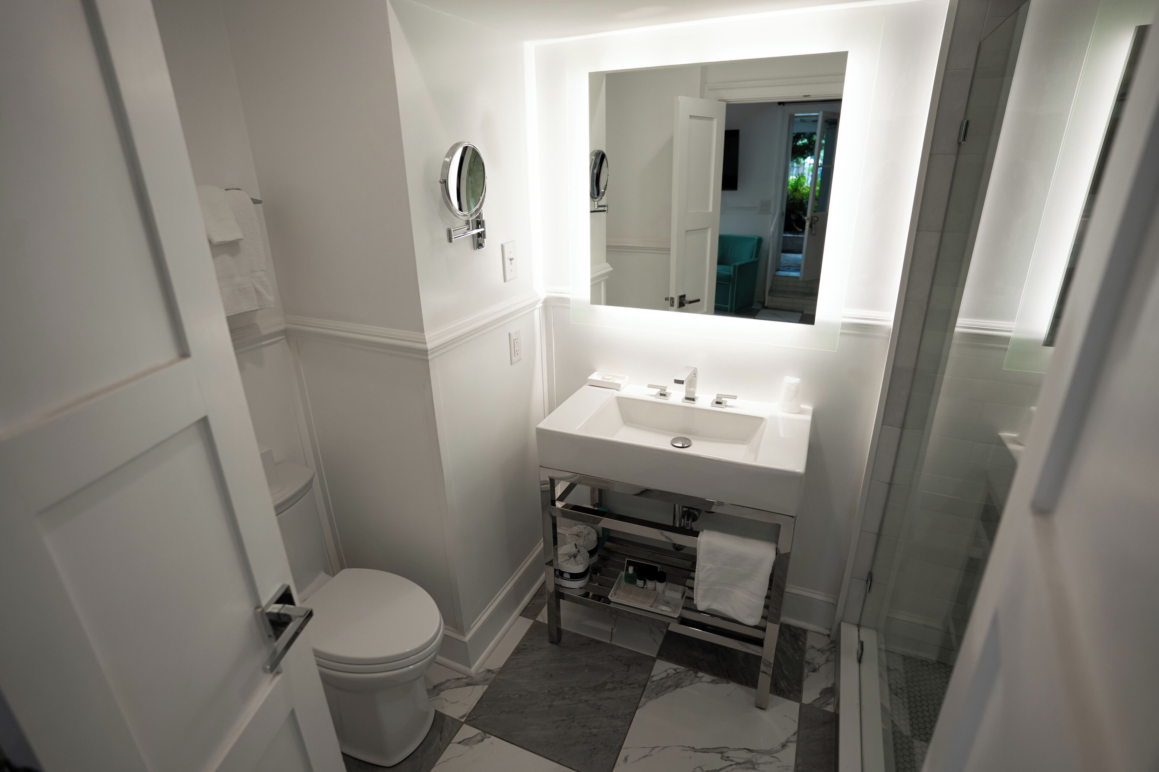 Une petite salle de bain avec des toilettes blanches, un lavabo surmonté d’un miroir et un espace douche.