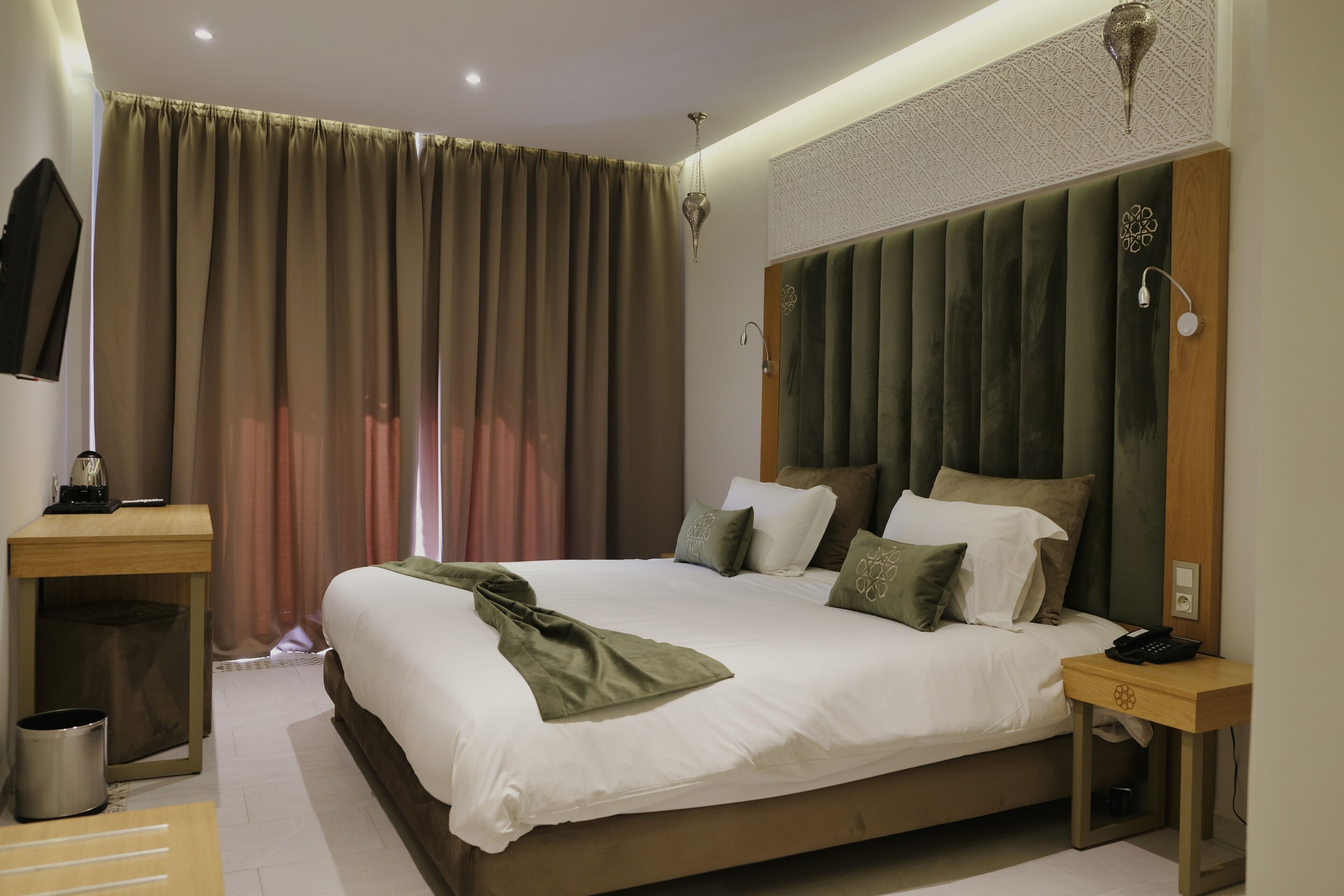 Une chambre d’hôtel moderne avec un grand lit, une table de chevet en bois, une petite table et un téléviseur fixé au mur.