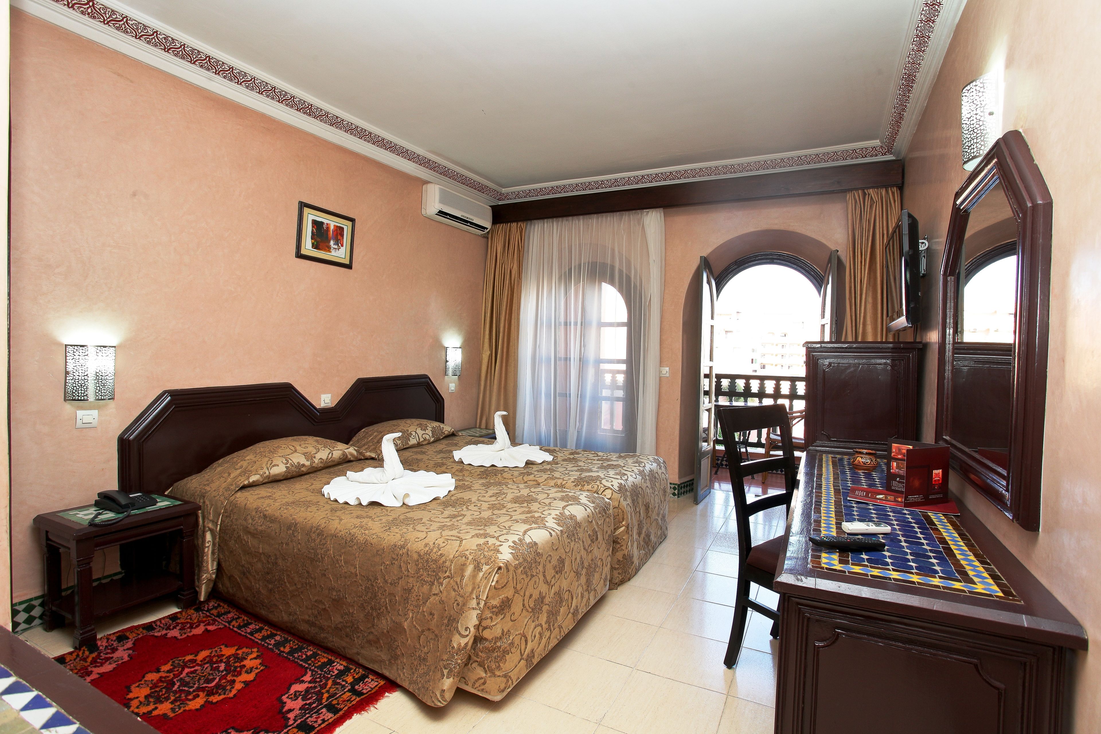 Une chambre d’hôtel avec un grand lit, un bureau avec un miroir, un téléphone et un tapis rouge.
