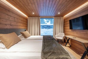 Una habitación tipo cabaña con paredes de madera, una cama, un escritorio y un televisor.