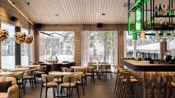 A restaurant with a bar area, wooden ceiling, and large windows with a view of trees.
