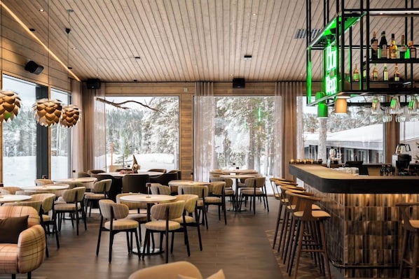 A restaurant with a bar area, wooden ceiling, and large windows with a view of trees. - Hotelli Kieppi (Saariselka)