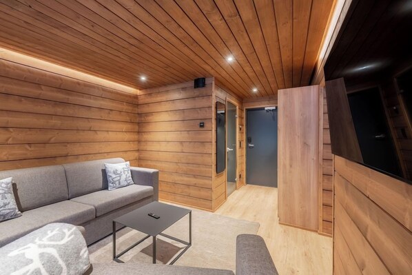 Un interior moderno con techo de listones de madera, un sofá con cojines estampados, una mesita y una puerta que da a otra habitación.