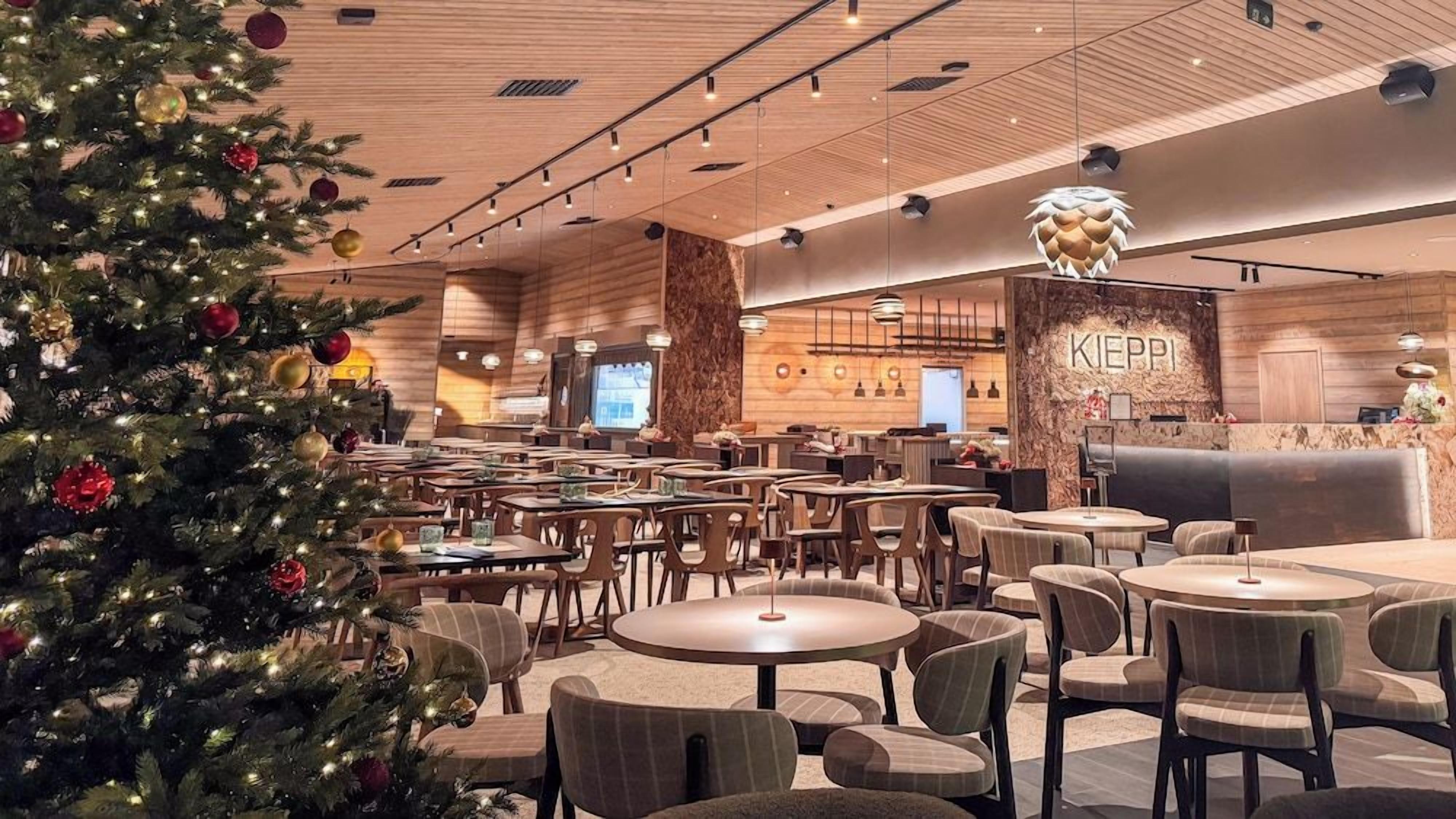 A spacious indoor area with multiple round tables and chairs, a Christmas tree, and a reception desk with the name 'KIEPI' on the wall.