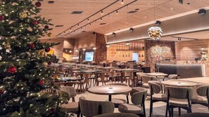 A spacious indoor area with multiple round tables and chairs, a Christmas tree, and a reception desk with the name 'KIEPI' on the wall. - Hotelli Kieppi (Saariselka)