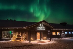 Mökki, jossa on puinen ulkoverhous, selkeästi näkyvä sisäänkäynti ja kyltti, jossa lukee: ”KIEPPI Wilderness Hotel”.