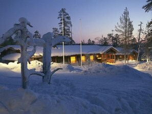 Una cabaña cubierta de nieve con fachada de madera y entrada iluminada.