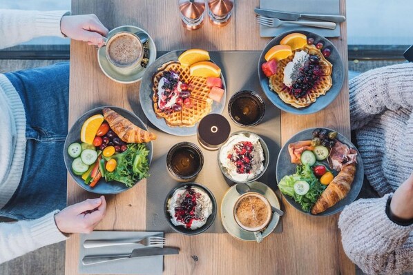 Una mesa con diferentes alimentos y bebidas, como waffles, fruta y un croissant.