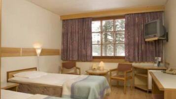 A hotel room with two single beds, a desk, a chair, a television, and a window with curtains.