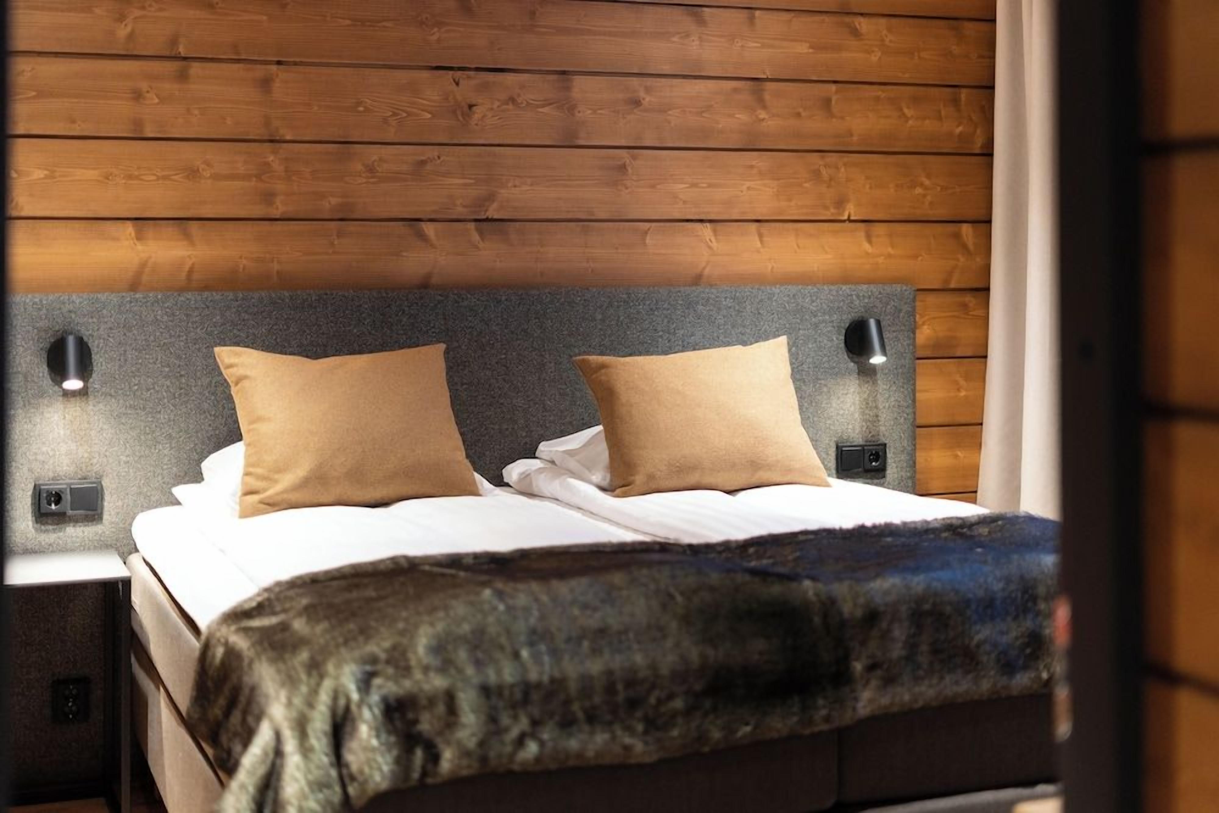 A bed with a headboard, two pillows, a blanket, and two bedside lamps.