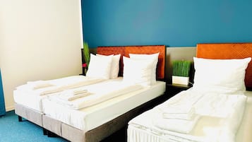 Habitación de hotel con dos camas, cada una con sábanas y almohadas blancas, alfombra azul y pared azul.